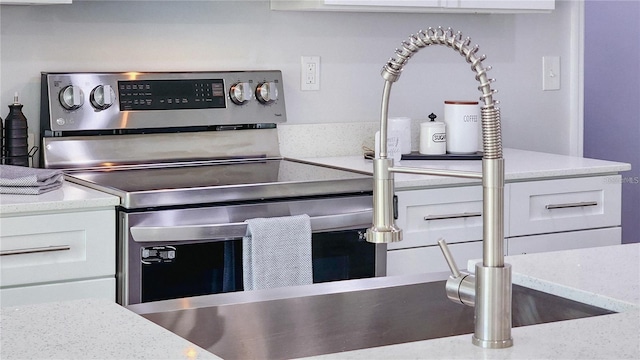 interior details featuring white cabinets, stainless steel electric range, and light stone countertops