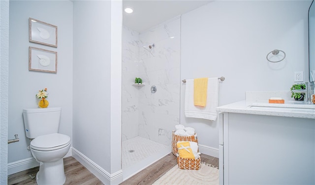 bathroom featuring wood-type flooring, vanity, toilet, and tiled shower