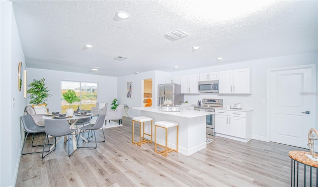 kitchen with stainless steel appliances, light hardwood / wood-style floors, white cabinetry, and an island with sink