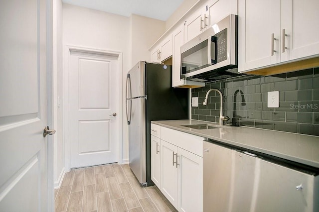 kitchen featuring stainless steel appliances, decorative backsplash, sink, white cabinets, and light hardwood / wood-style flooring