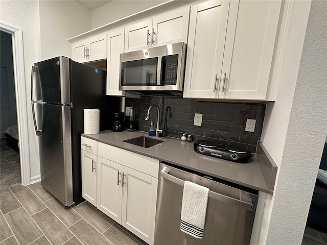 kitchen with stainless steel appliances, white cabinetry, sink, backsplash, and light hardwood / wood-style flooring