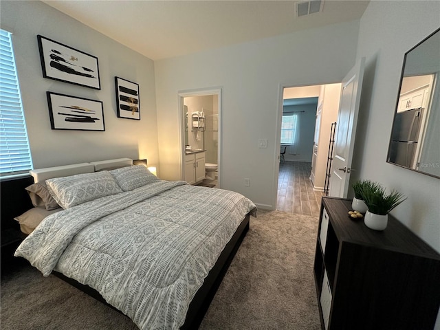 bedroom with ensuite bathroom, hardwood / wood-style floors, and stainless steel fridge