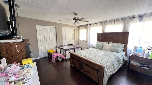 bedroom with dark wood-type flooring, ceiling fan, a textured ceiling, and multiple closets