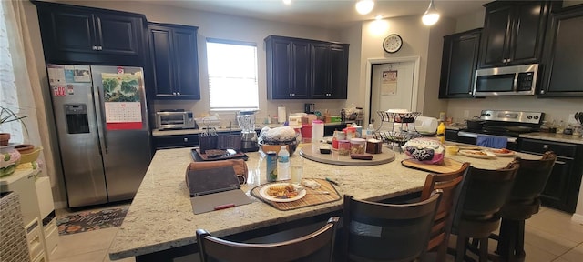 kitchen with stainless steel appliances, light stone counters, light tile patterned floors, and a kitchen island