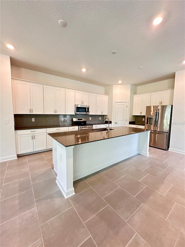 kitchen with decorative backsplash, appliances with stainless steel finishes, light tile patterned floors, a center island with sink, and white cabinetry