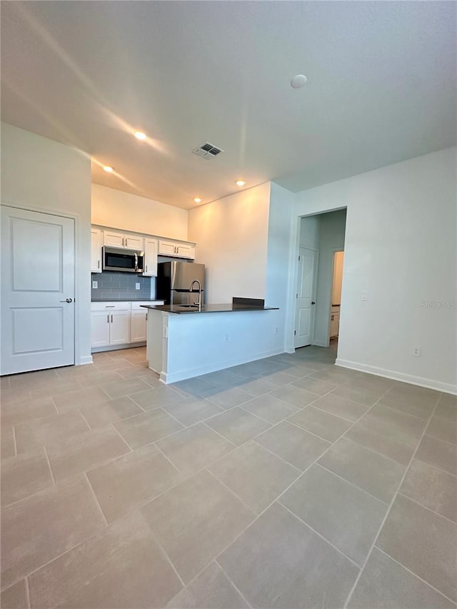 kitchen with light tile patterned flooring, kitchen peninsula, decorative backsplash, white cabinets, and appliances with stainless steel finishes