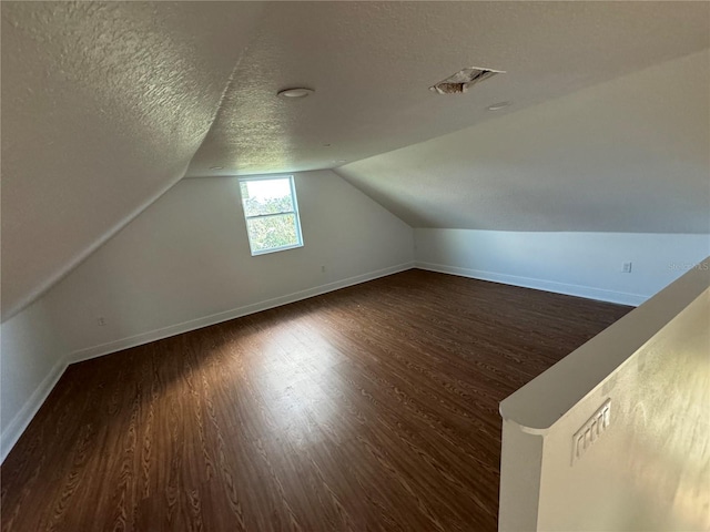 bonus room featuring vaulted ceiling, dark wood-type flooring, and a textured ceiling