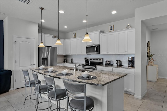 kitchen with stainless steel appliances, sink, white cabinetry, hanging light fixtures, and an island with sink