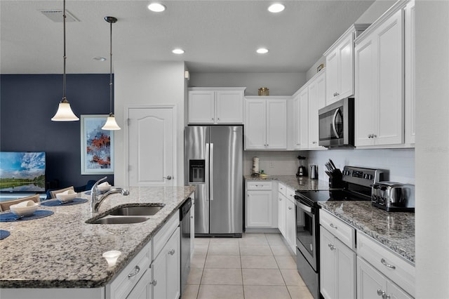 kitchen with white cabinetry, sink, hanging light fixtures, stainless steel appliances, and a center island with sink