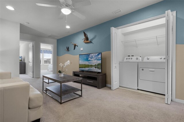 living room featuring independent washer and dryer, light colored carpet, and ceiling fan