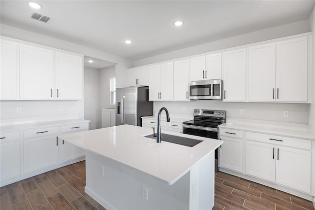 kitchen with white cabinets, appliances with stainless steel finishes, a kitchen island with sink, and sink