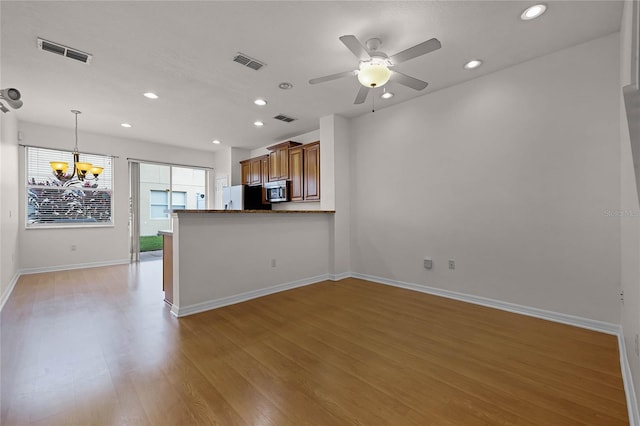 unfurnished living room featuring ceiling fan with notable chandelier and light hardwood / wood-style flooring