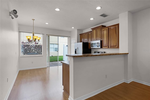 kitchen featuring kitchen peninsula, pendant lighting, stainless steel appliances, and light hardwood / wood-style floors