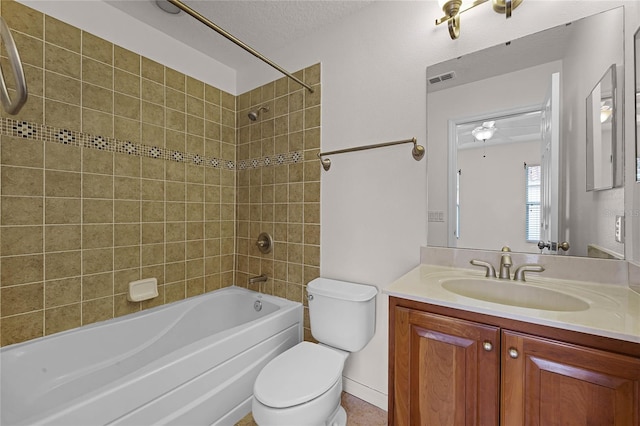 full bathroom with ceiling fan, tiled shower / bath combo, a textured ceiling, toilet, and vanity