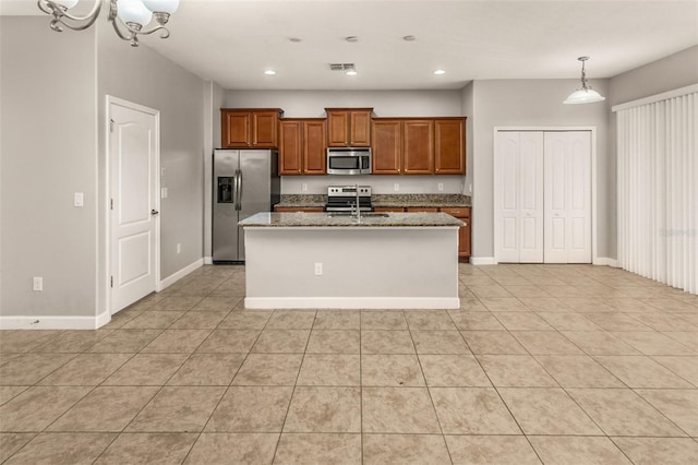 kitchen featuring hanging light fixtures, sink, light stone countertops, an island with sink, and appliances with stainless steel finishes