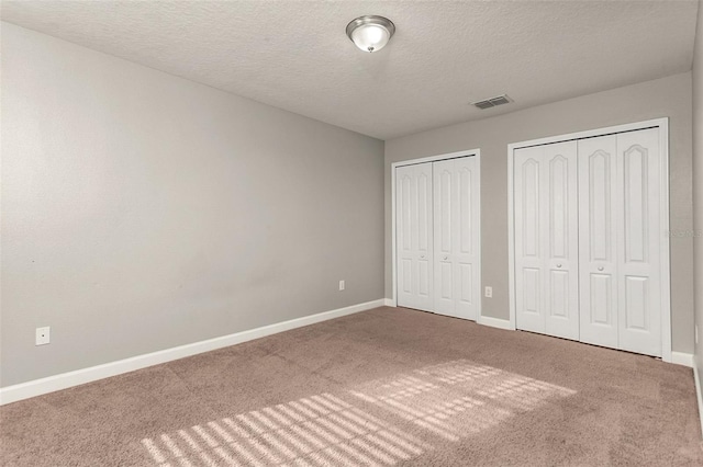 unfurnished bedroom with carpet flooring, a textured ceiling, and two closets