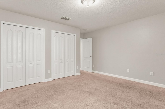 unfurnished bedroom featuring a textured ceiling, light carpet, and two closets