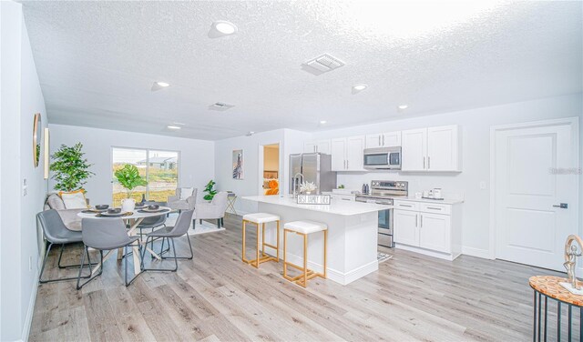 kitchen with stainless steel appliances, white cabinetry, a kitchen island with sink, and light hardwood / wood-style flooring