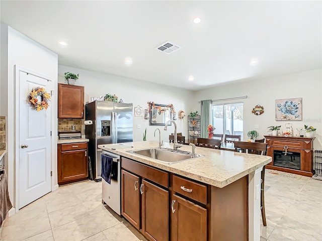 kitchen with sink, backsplash, a kitchen island with sink, light tile patterned flooring, and appliances with stainless steel finishes