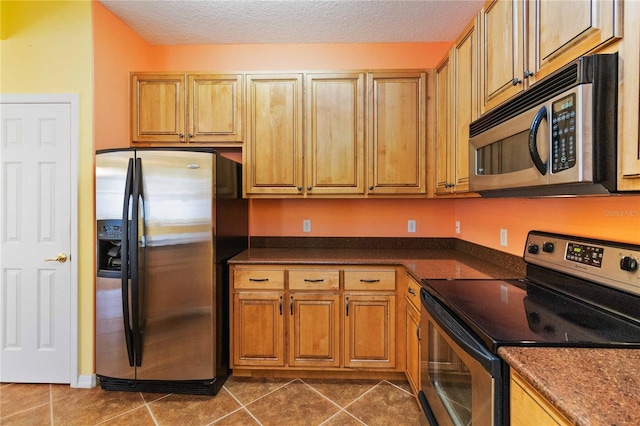 kitchen with a textured ceiling, stainless steel appliances, and dark tile patterned flooring