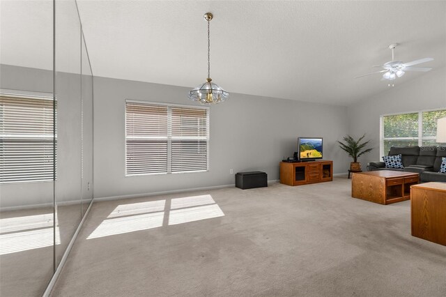 unfurnished living room featuring ceiling fan with notable chandelier, vaulted ceiling, and light carpet