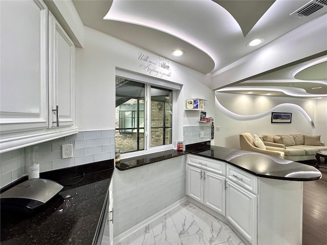 kitchen with light hardwood / wood-style flooring, backsplash, kitchen peninsula, dark stone countertops, and white cabinets