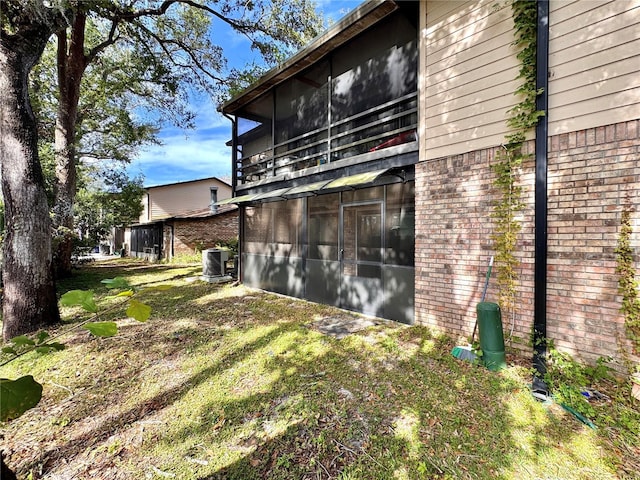 view of side of property featuring a sunroom, a yard, and central AC