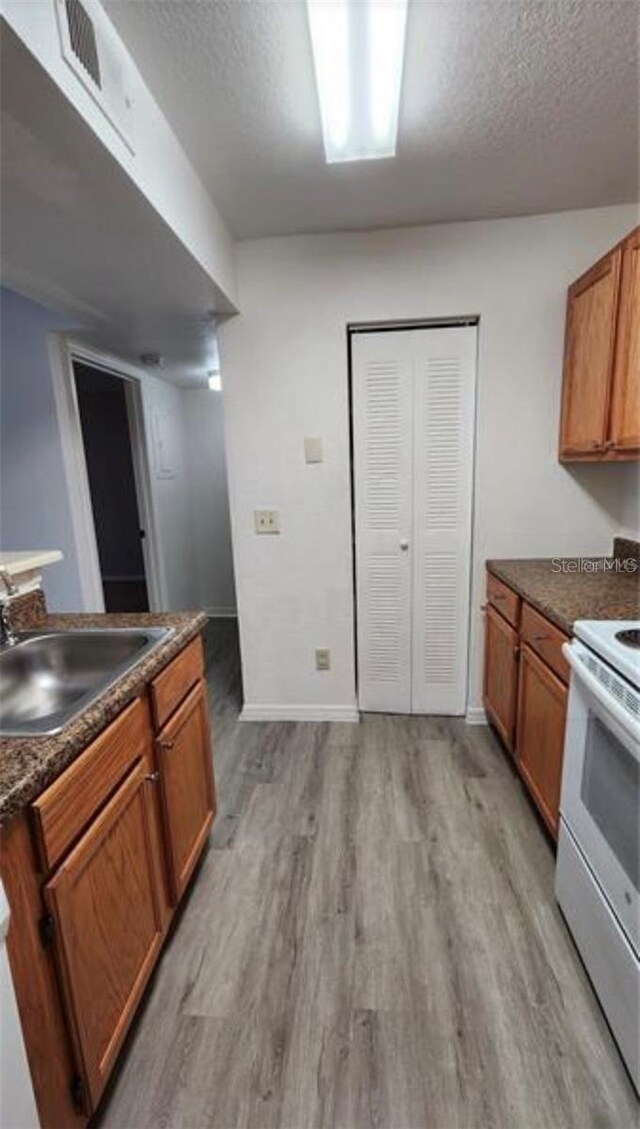 kitchen featuring a textured ceiling, light hardwood / wood-style floors, white range with electric stovetop, and sink