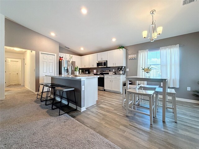 kitchen with stainless steel appliances, decorative light fixtures, lofted ceiling, a kitchen island with sink, and white cabinets