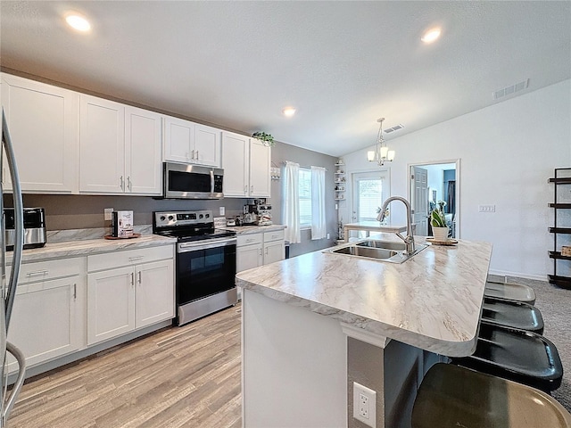 kitchen featuring appliances with stainless steel finishes, vaulted ceiling, sink, hanging light fixtures, and an island with sink