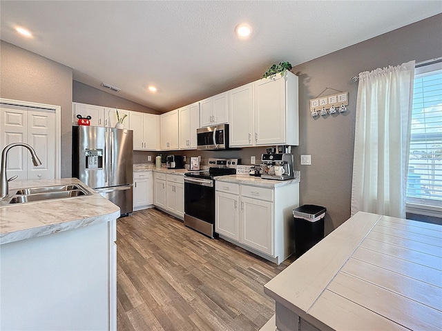 kitchen with lofted ceiling, sink, light hardwood / wood-style flooring, white cabinetry, and stainless steel appliances