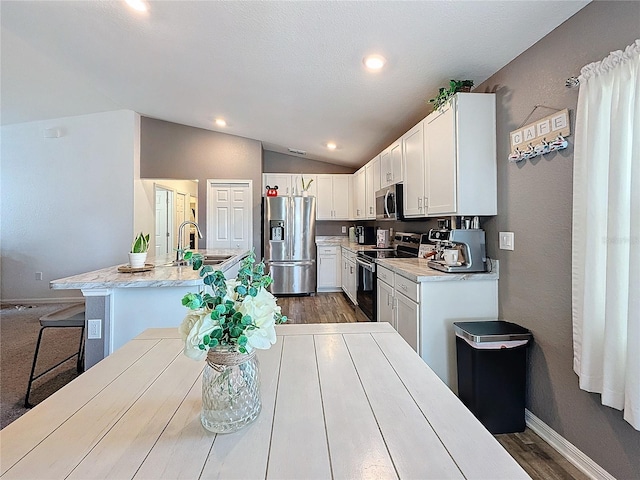 kitchen with stainless steel appliances, vaulted ceiling, sink, white cabinets, and an island with sink