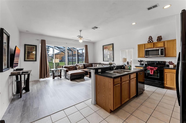 kitchen featuring ceiling fan, sink, black appliances, light hardwood / wood-style flooring, and an island with sink