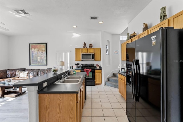 kitchen with sink, a kitchen island with sink, light tile patterned floors, black appliances, and a textured ceiling