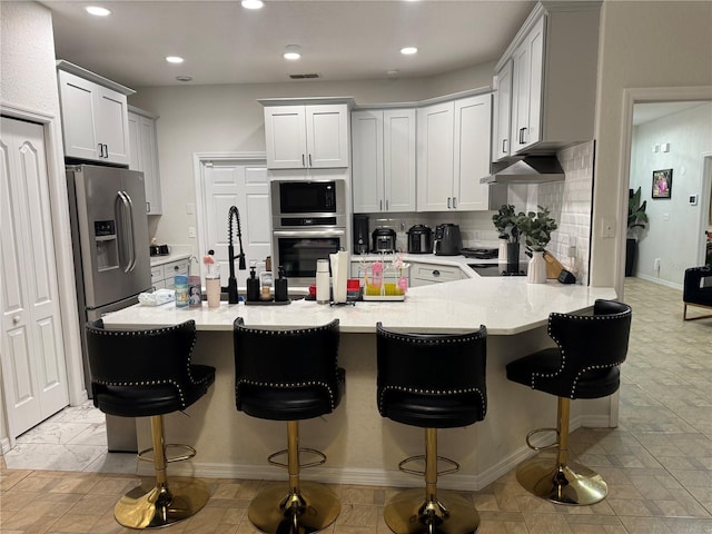 kitchen featuring white cabinetry, tasteful backsplash, a breakfast bar area, kitchen peninsula, and stainless steel appliances