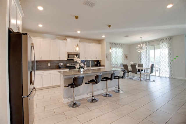 kitchen with stainless steel appliances, an island with sink, decorative light fixtures, a kitchen bar, and white cabinets