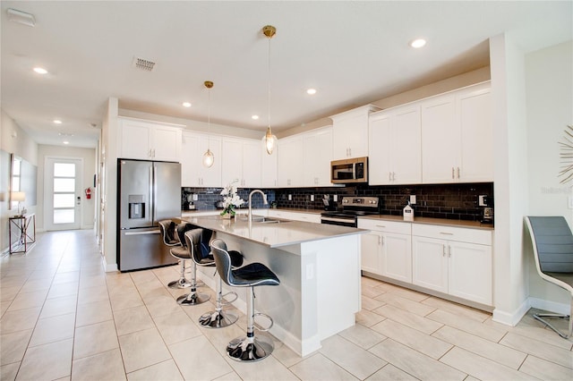 kitchen with stainless steel appliances, sink, decorative light fixtures, a center island with sink, and white cabinetry