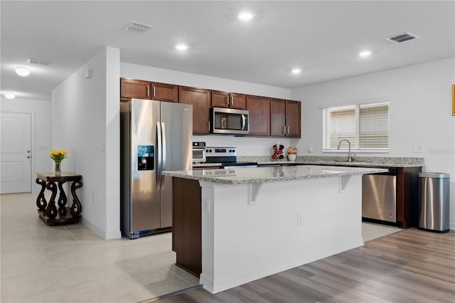 kitchen featuring a kitchen breakfast bar, light stone counters, stainless steel appliances, light hardwood / wood-style floors, and a kitchen island