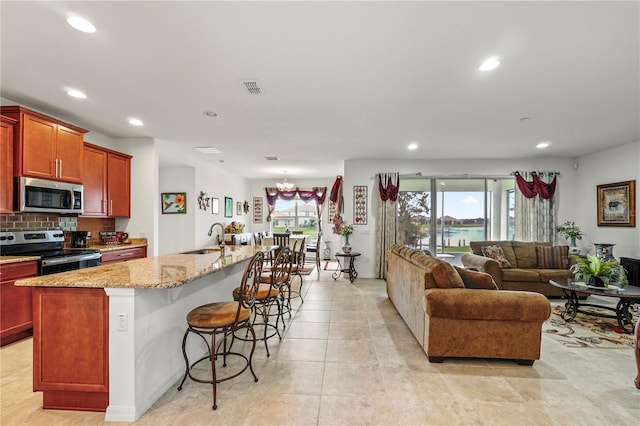 kitchen with sink, tasteful backsplash, a breakfast bar area, a center island with sink, and appliances with stainless steel finishes