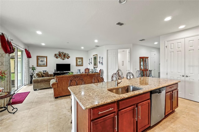 kitchen with sink, light stone counters, stainless steel dishwasher, and an island with sink