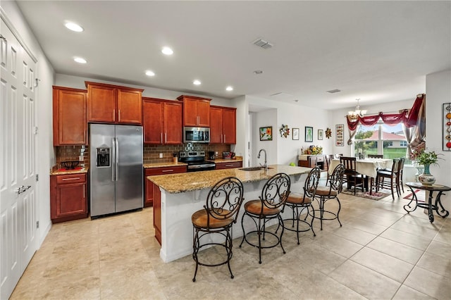 kitchen with light stone countertops, appliances with stainless steel finishes, sink, a center island with sink, and a breakfast bar area