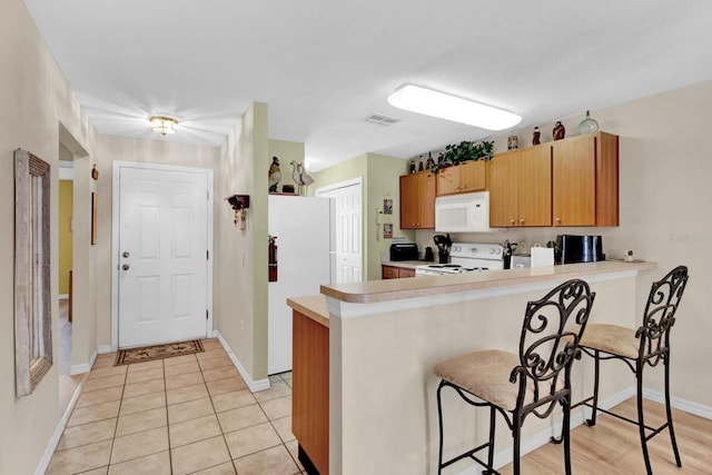 2216 Mystic Ring Loop, Poinciana, FL 34759 - kitchen featuring white appliances, a peninsula, light countertops, a kitchen bar, and light tile patterned floors