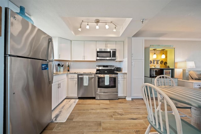 kitchen featuring ornamental molding, a tray ceiling, light hardwood / wood-style floors, white cabinetry, and stainless steel appliances