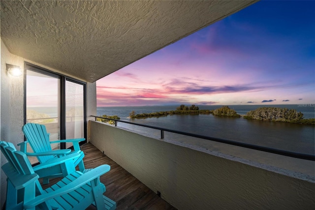 balcony at dusk featuring a water view