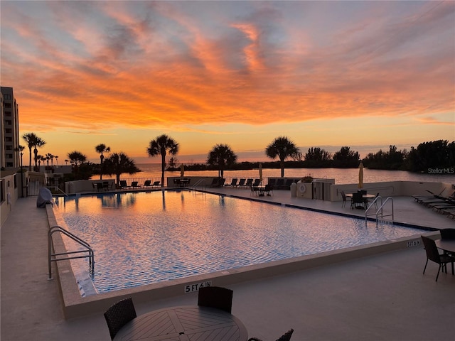 pool at dusk with a patio area and a water view