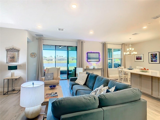 living room with light hardwood / wood-style flooring, a water view, and a notable chandelier