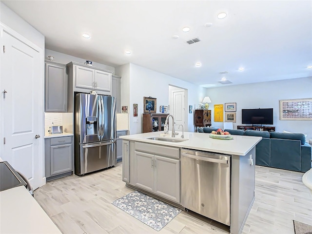 kitchen with stainless steel appliances, a center island with sink, gray cabinetry, and sink