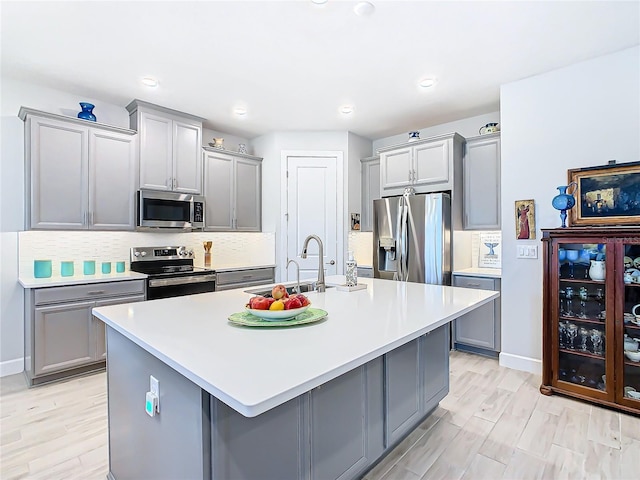 kitchen featuring decorative backsplash, appliances with stainless steel finishes, sink, a center island with sink, and gray cabinets