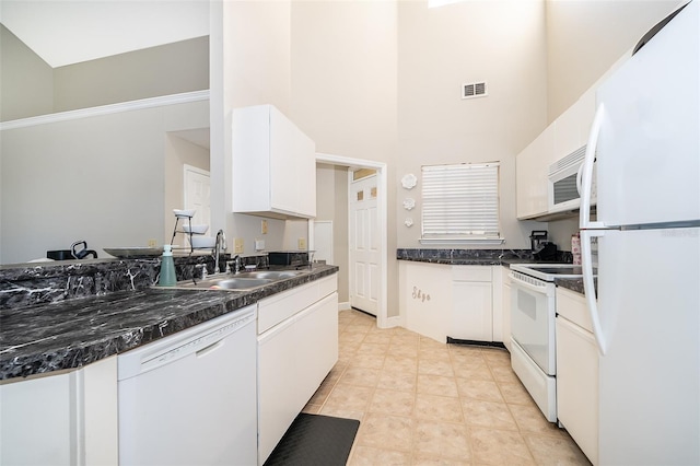 kitchen featuring white appliances, white cabinets, sink, dark stone countertops, and a towering ceiling