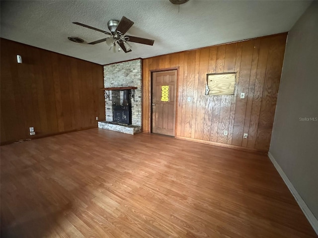 unfurnished living room featuring a textured ceiling, light hardwood / wood-style flooring, ceiling fan, and wooden walls